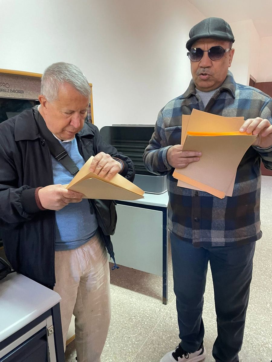 Deux membres de l'équipe AMARDEV examinent des pochettes de documents, près d'une machine à gaufrer le braille