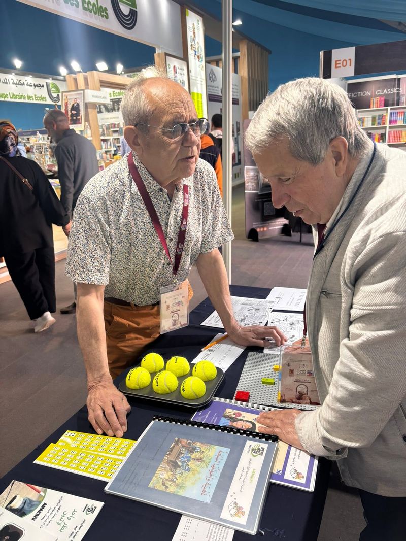 Deux visiteurs examinent des jeux tactiles en braille (balles de tennis, briques LEGO) sur le stand AMARDEV