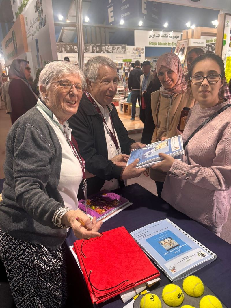 Des bénévoles AMARDEV présentent un livret à deux jeunes visiteuses sur le stand