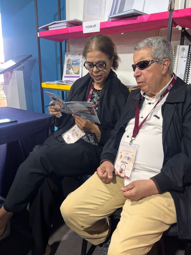 Deux personnes assises consultent ensemble un livret illustré sur le stand du salon
